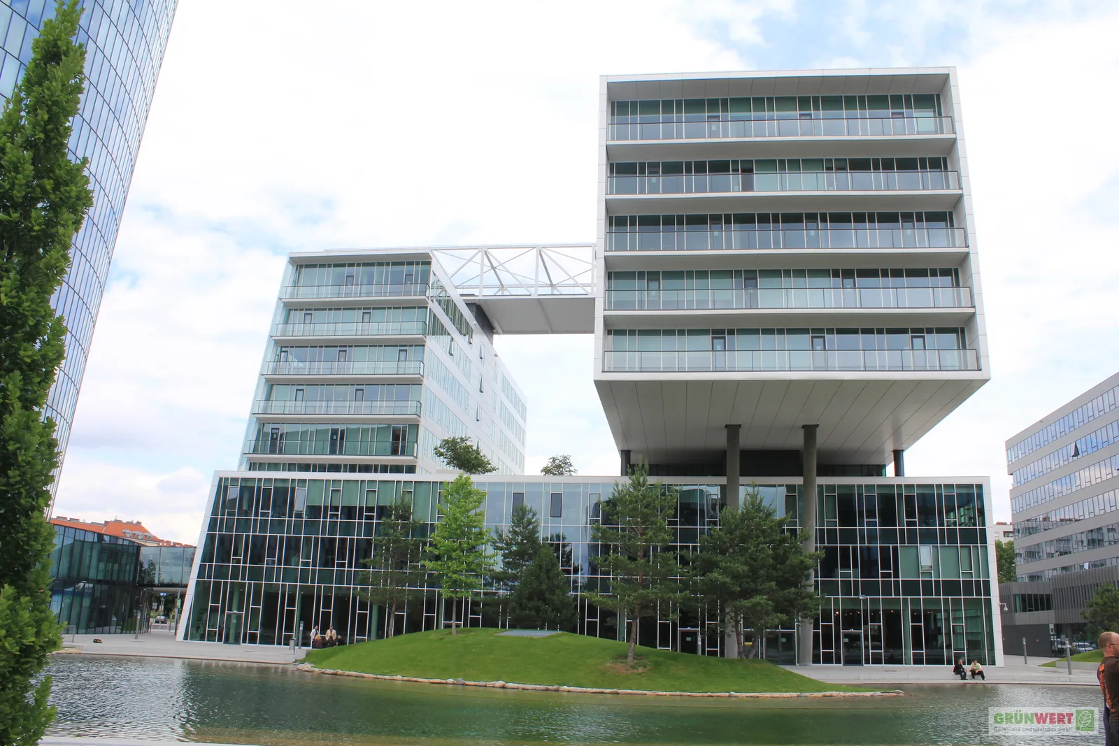 Bürogebäude am Wasserbecken mit Rasenhügel und jungen Nadelbäumen