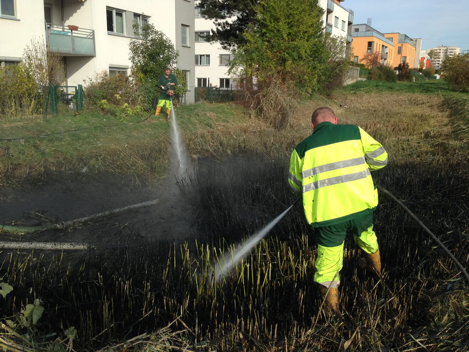 Zwei Mitarbeiter in Warnkleidung spülen ein verschlammtes Becken mit Wasserstrahl