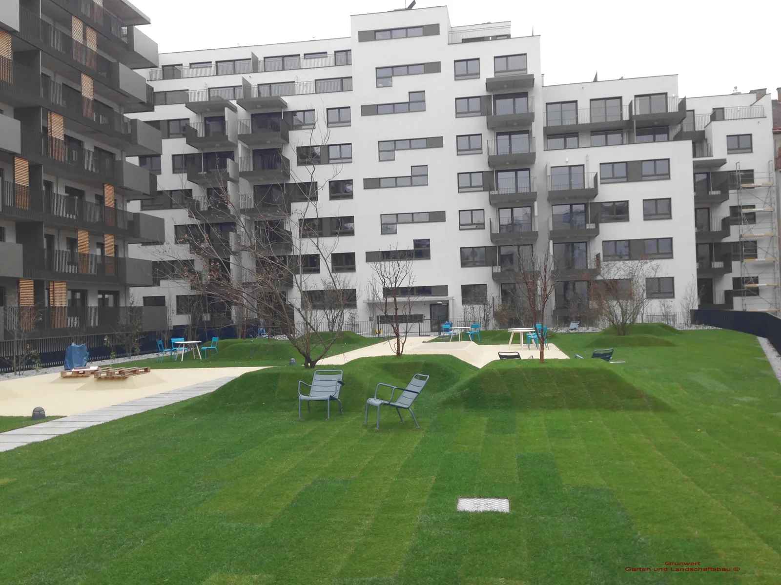 Innenhof einer Wohnhausanlage mit frisch verlegtem Rollrasen, Hügeln und Sitzmöbeln