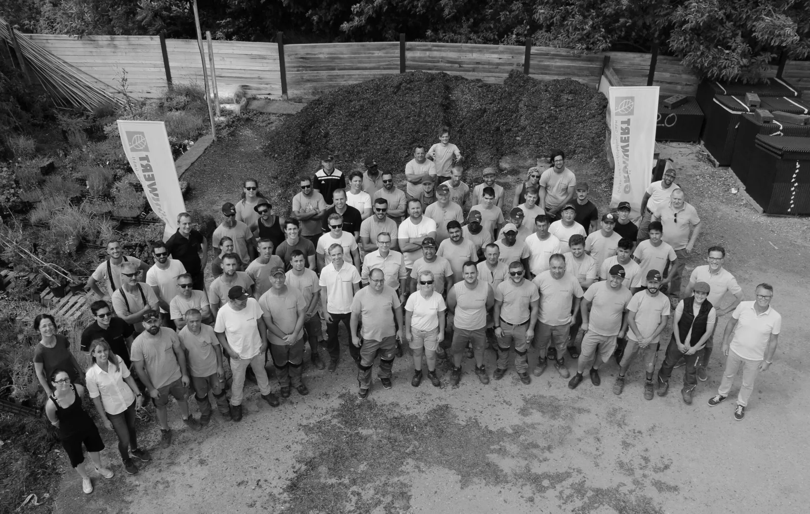 Gruppenfoto der ganzen Grünwert-Belegschaft von oben, zwischen zwei Grünwert-Fahnen, schwarzweiß